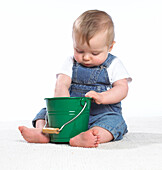 Baby boy sitting on floor with one hand in green bucket
