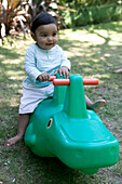Baby girl in garden sitting on plastic green toy vehicle