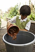 Elementary boy filling large plastic bin with broken pots