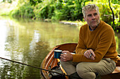 Man with coffee fly fishing in boat on river
