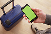 Person holding a phone with a green screen near a suitcase