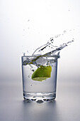 Lime wedge splashing into glass of water