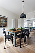 Industrial style pendant lamp above a wooden farmhouse dining table and black dining chairs