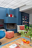 Seating in front of a fireplace in an open living room with blue wall, bookcase in the background