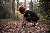 Young female runner tying shoelace in autumn woods