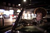 Young woman using smartphone in convertible at night