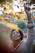 Happy young woman reaching for autumn leaves on tree branch