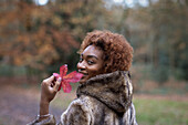 Happy young woman with red autumn leaf in park