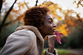 Thoughtful young woman with red autumn leaf in park