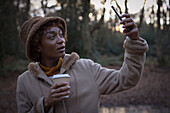 Young woman with coffee taking selfie in park