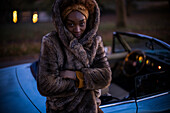 Young woman in fur coat outside convertible at night