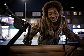 Happy young woman outside convertible at night
