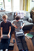 Teenage brothers home schooling at laptops in living room