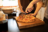 Boys slicing homemade pizza on cutting board in kitchen