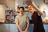 Happy teenage boys laughing and taking selfie in kitchen