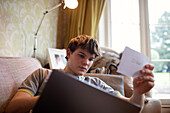 Teenage boy with laptop studying in living room