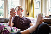 Teenage boy using smartphone at on living room sofa