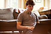 Focused teenage boy using laptop on living room floor