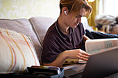 Teenage boy with textbook and laptop studying at home
