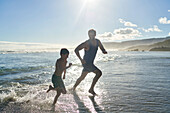Happy father and son running in sunny ocean surf