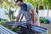 Father and daughter watering plants in backyard
