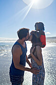 Affectionate couple with daughter kissing on sunny beach