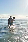 Happy father and son playing in sunny summer ocean