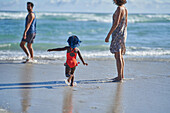 Toddler girl playing in sunny ocean surf with parents