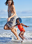Happy mother and toddler daughter running in ocean surf