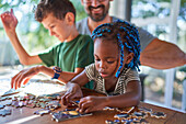 Toddler girl assembling jigsaw puzzle with family at table