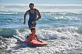 Happy father and son body boarding in sunny ocean surf
