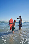 Father and son with body board wading in sunny ocean surf