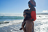 Mother carrying toddler daughter on shoulders on beach