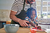 Father helping daughter slice fruit at home