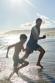 Happy father and son running in sunny summer ocean surf