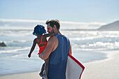 Father carrying toddler daughter on sunny summer ocean beach