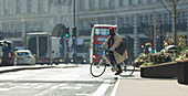 Commuter riding bicycle on sunny city street, London, UK