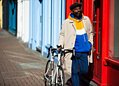 Man walking with bicycle along sunny storefronts