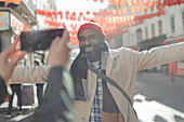 Woman photographing happy man on sunny city street