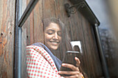 Smiling young woman with smartphone in window