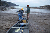 Young couple pulling canoe on beach, Kent, UK