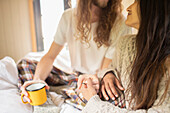 Affectionate young couple with coffee holding hands in bed