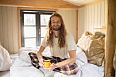 Happy young man in pyjamas drinking coffee in bed