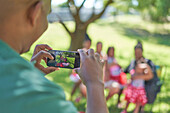Man photographing family with smartphone in park