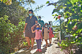 Family in face masks walking on sunny summer path