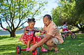 Grandfather helping granddaughter ride tricycle in park