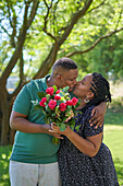 Affectionate couple with rose bouquet kissing in park