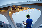 Man in helmet using digital tablet below illuminated bridge