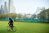 Young man riding bicycle in urban park, London, UK