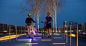 Men with bicycles on illuminated path in city at night